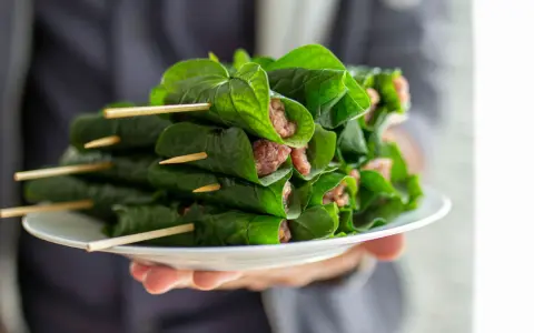 Bo la lot, ein vietnamesisches Gericht, auf einem Teller präsentiert. Fleisch ist in grüne Blätter gewickelt und mit Holzspießen fixiert.