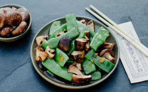 Gebratene Thai Bohnen mit Pilzen in einer dunklen Soße, serviert mit Stäbchen.