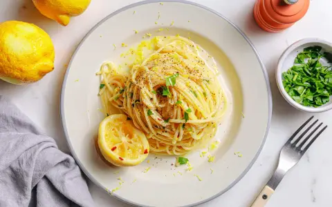 Vegane Pasta mit Zitronenschale und Kräutern, garniert mit einer Zitronenhälfte und frisch gemahlenem Pfeffer.