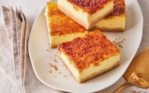 Köstliche Stücke Creme Brulee Kuchen mit karamellisierter Zuckerkruste auf einem Teller, daneben eine goldene Tortenheber.