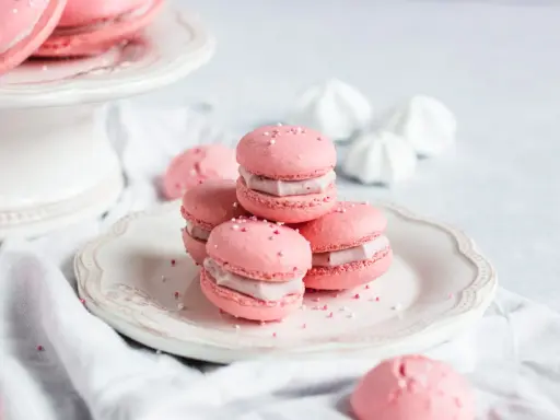Rosa Macarons mit Himbeer-Ganache-Füllung, bestreut mit Zuckerperlen, auf einem Teller.