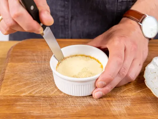 Ein Messer löst den Rand eines cremigen Flan Puddings in einer weißen Keramikschale.