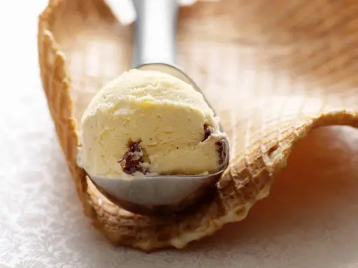 Ein Löffel cremiges Malaga Eis mit Rosinen, bereit für ein Waffelhörnchen. Ein einfaches Malaga Eis Rezept für den Sommer.