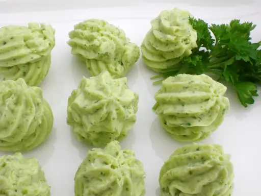 Grüne Kräuterbutter-Tuffs auf weißer Platte, perfekt für Ihre butter rezepte. Frische Petersilie daneben.