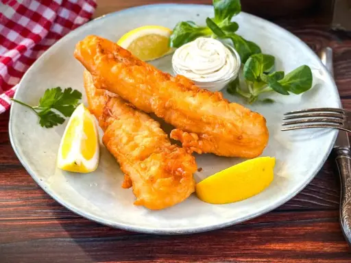 Zwei goldbraun frittierter Fisch mit Zitronenspalten, Sauce und Salat auf einem Teller.