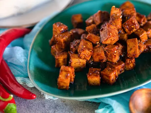 Würzig gebratene Tofuwürfel auf einem grünen Teller, daneben rote Chilis. So schmeckt Tofu!