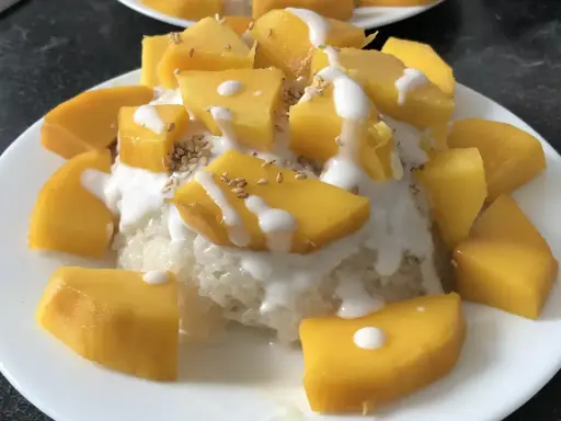 Ein Teller mit Klebreis, garniert mit saftigen Mango-Stücken, Kokosmilch und Sesam. Ein köstlicher **thai dessert mango**.
