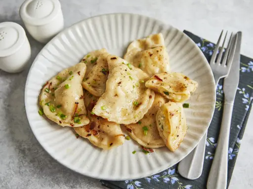 Hausgemachte Tworog Rezepte: goldbraune Teigtaschen, gefüllt mit Quark, bestreut mit Schnittlauch und Röstzwiebeln.