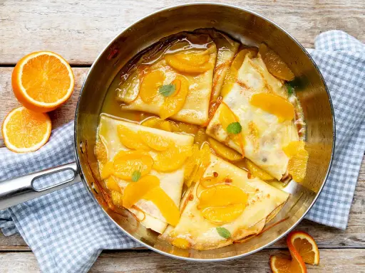 Crêpes Suzette im Originalrezept: zarte Pfannkuchen in Orangensauce mit frischen Orangenspalten und Minze garniert.