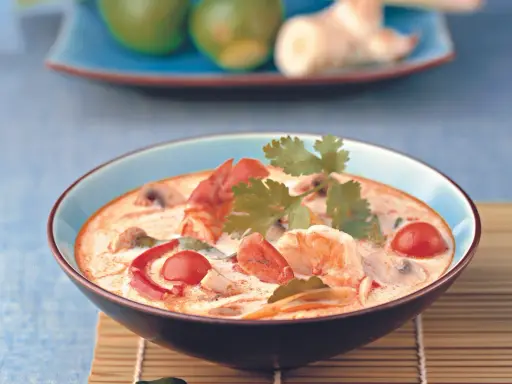 Eine cremige garnelensuppe asiatisch mit Garnelen, Pilzen und Tomaten, garniert mit Koriander.