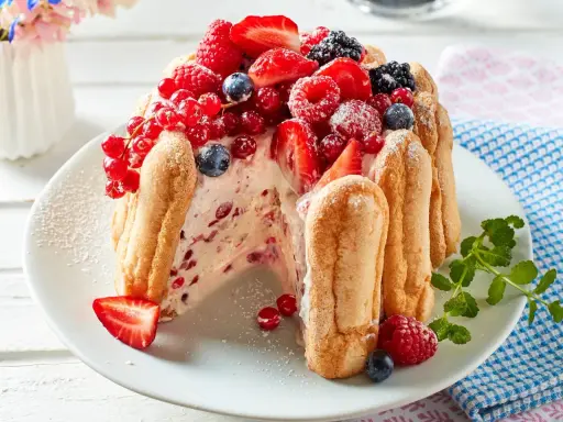 Eine köstliche Charlotte Torte, umhüllt von Löffelbiskuits und üppig belegt mit frischen Beeren wie Erdbeeren, Himbeeren und Johannisbeeren.