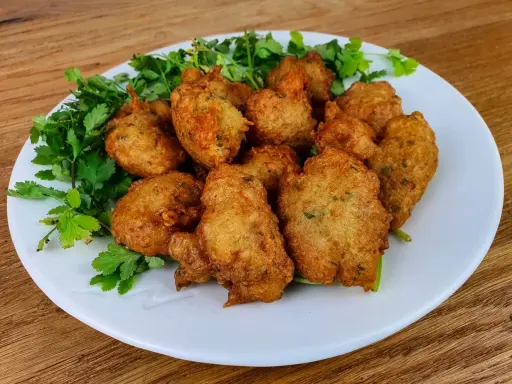 Knusprige Accras de Morue, goldbraun frittiert und mit frischer Petersilie garniert, auf einem weißen Teller.