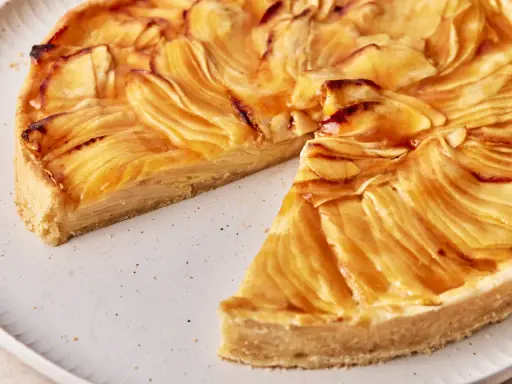Eine köstliche Tarte au Pomme mit karamellisierten Apfelscheiben auf einem knusprigen Boden, auf einem rustikalen Teller.