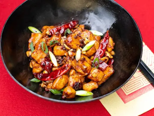 Ein köstliches Gericht mit asiatischen Rezepten mit Huhn, garniert mit Chilis und Frühlingszwiebeln in einer schwarzen Schüssel.