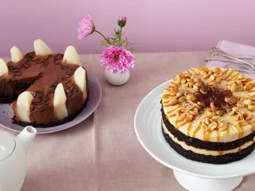 Zwei Torten auf einem Tisch: eine Schokoladen-Birnen-Torte und eine köstliche Erdnuss Torte mit Karamell und Nüssen.
