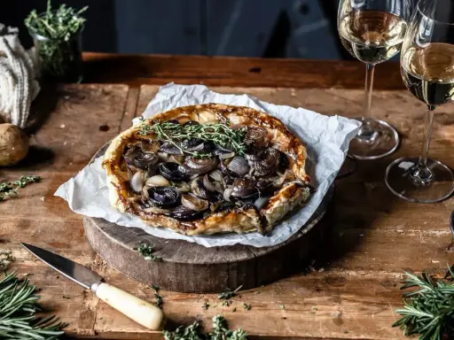 Herzhafte Tarte Tatin mit karamellisierten Zwiebeln und frischen Kräutern, serviert mit Weißwein.