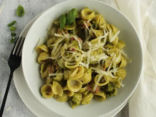 Orecchiette-Pasta mit grünem Pesto, Speck und geriebenem Parmesan. Ein köstliches Gericht, das zeigt, wie vielseitig Rezepte mit Pistazienmus sein können.