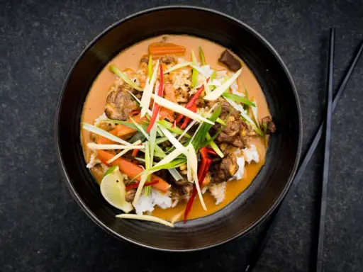 Ein aromatischer Thai Curry Rind mit Reis, Karotten und frischen Kräutern, garniert mit Limette.