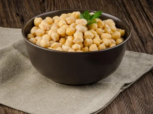 Schüssel mit Kichererbsen, die auf einem Leinentuch auf Holzhintergrund steht. Keine Sorge, Kichererbsen aus der Dose sind nicht giftig!