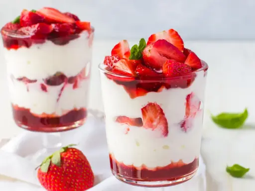 Zwei Gläser mit Erdbeer Mascarpone Creme, geschichtet mit frischen Erdbeeren und Erdbeersauce, garniert mit Minze.