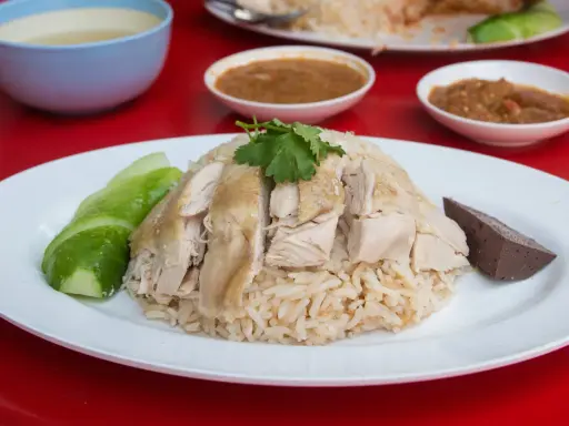 Khao Man Gai: gedämpfter Reis mit zartem Hühnchen, Gurkenscheiben und einer Blutwurstscheibe, garniert mit Koriander.