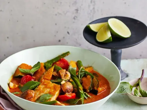 Ein köstliches Panang Curry mit Fisch, Kürbis, grünen Bohnen und Tomaten, garniert mit frischem Basilikum und Limettenspalten.