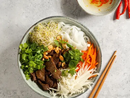 Bun bo nam bo: Reisnudeln, Rindfleisch, Sprossen, Karotten, Kohl und Kräuter in einer Schüssel, garniert mit Erdnüssen.