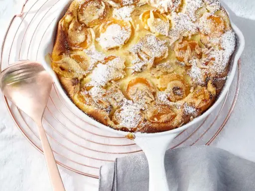 Ein goldbrauner Aprikosen Clafoutis, bestäubt mit Puderzucker und Mandelsplittern, wartet auf seine Verkostung.
