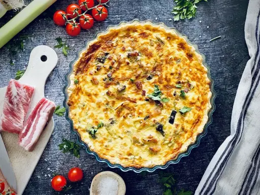 Herzhafte Quiche mit Speck und Lauch, perfekt für herzhafte Quiche Rezepte. Dazu frische Tomaten und Kräuter.