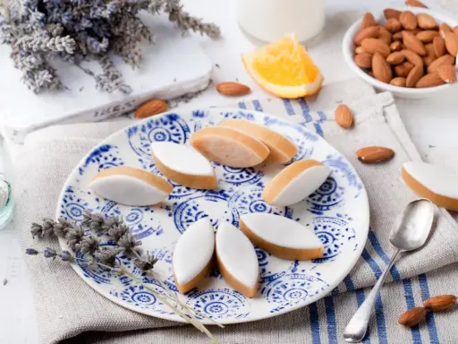Calissons rezept: Süße Mandelkekse mit weißer Glasur auf blau-weißem Teller, garniert mit Lavendel und Mandeln.