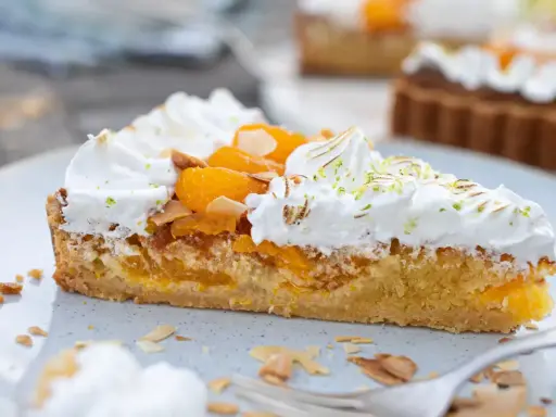 Ein Stück Mandarinen Tarte mit Baiserhaube, Mandelsplittern und frischer Zitronenschale bestreut.