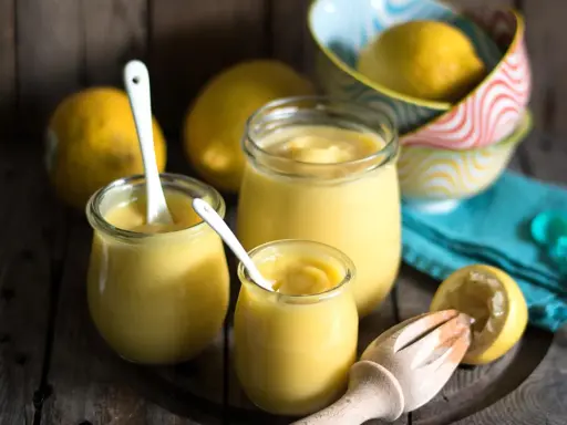 Leichte Zitronencreme im Thermomix zubereitet, serviert in Gläsern mit Löffeln, daneben frische Zitronen und ein Zitruspresse.