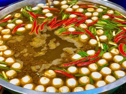Ein dampfender Topf mit Fleischbällchen, Chilis und Frühlingszwiebeln – ein Einblick in die vielfältigen Esskulturen weltweit.