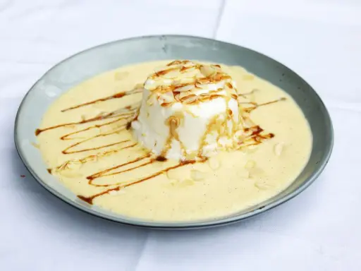 Ein leichtes, schwebendes Dessert aus Eischnee, umgeben von cremiger Vanillesauce, garniert mit Mandelsplittern und Karamell.