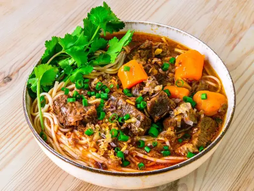 Herzhaftes Bo Kho mit zarten Rindfleischstücken, Karotten und Nudeln, garniert mit Koriander und Frühlingszwiebeln.