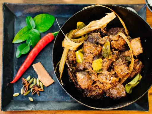 Ein dampfender Topf mit würzigem Beef Rendang, daneben frische Kaffirlimettenblätter, Chili und Gewürze.