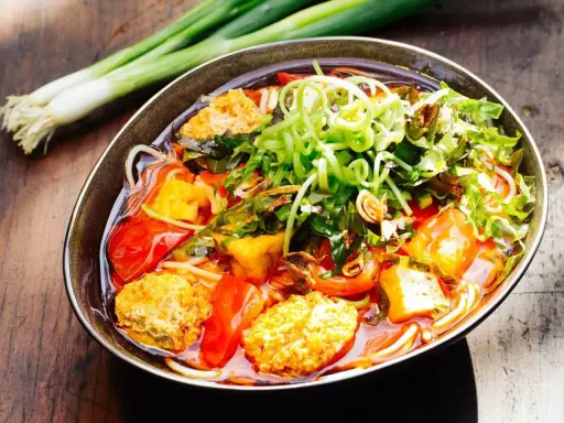 Herzhaftes Bun Rieu mit Tofu, Tomaten und frischen Kräutern, garniert mit Frühlingszwiebeln.