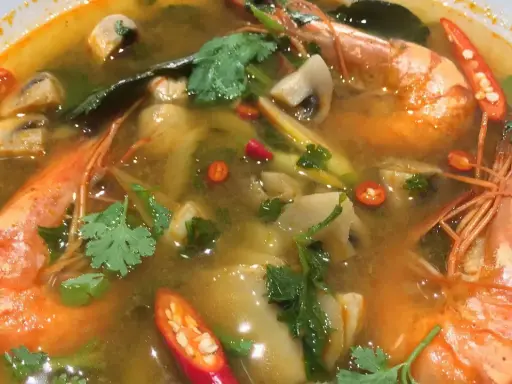 Eine dampfende Schüssel mit scharfer Thai Suppe, gefüllt mit Garnelen, Pilzen und Chili.