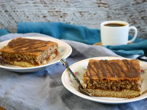 Zwei Stücke Blechkuchen mit Schokoladenglasur auf Tellern, perfekt, wenn man den Blechkuchen 3 Tage vorher backen möchte. Dazu eine Tasse Kaffee.