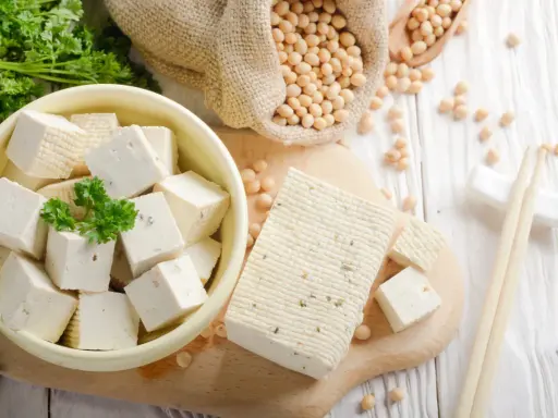 Frischer Tofu, ein toller Fleischersatz, liegt neben Sojabohnen und Petersilie.
