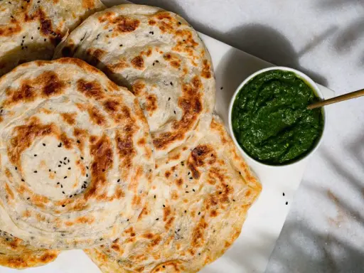 Fluffiger Roti Canai mit schwarzen Sesamkörnchen, daneben eine Schale mit grüner Chutney-Sauce.