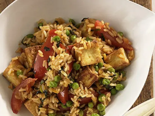 Herzhafter pilaw reis mit gebratenem Tofu, Erbsen und Tomatenstücken in einer weißen Schüssel.