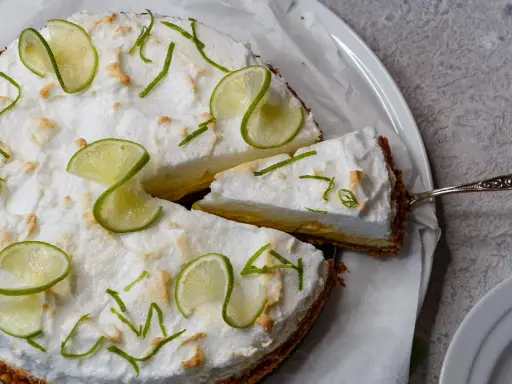 Eine köstliche Limetten Tarte mit luftiger Baiserhaube, garniert mit frischen Limettenscheiben und Zesten. Ein Stück wird gerade serviert.
