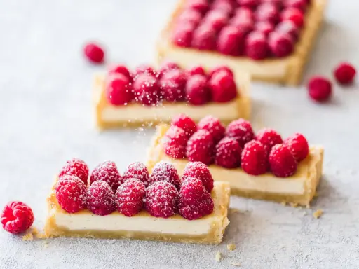 Drei rechteckige Tarte aux fruits mit frischen Himbeeren und Puderzucker bestreut.