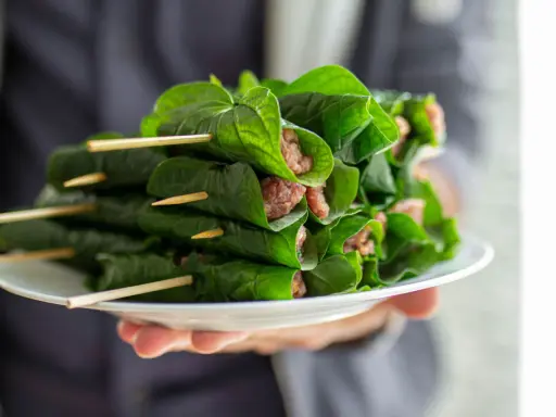 Bo la lot, ein vietnamesisches Gericht, auf einem Teller präsentiert. Fleisch ist in grüne Blätter gewickelt und mit Holzspießen fixiert.