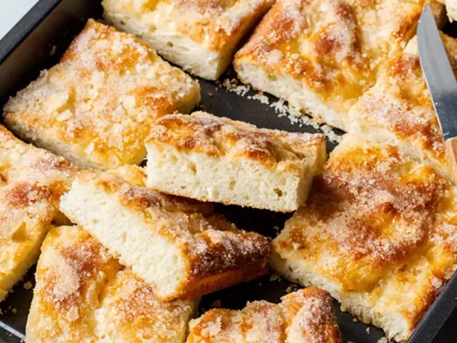 Ein Blech mit saftigem, **schneller Butter zuckerkuchen**, in Stücke geschnitten. Ein Messer liegt bereit.