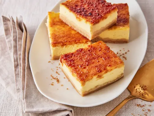 Köstliche Stücke Creme Brulee Kuchen mit karamellisierter Zuckerkruste auf einem Teller, daneben eine goldene Tortenheber.