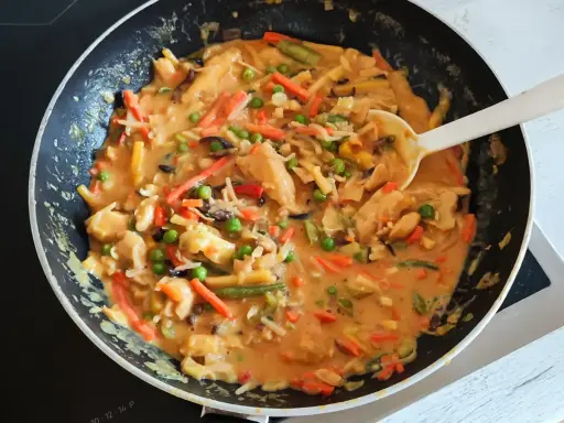 Ein köstliches veganes Curry mit viel Gemüse wie Karotten, Erbsen und Bambussprossen wird in einer Pfanne zubereitet.