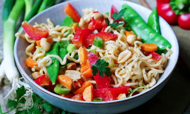 Schüssel mit Nudeln, Erdnüssen, Zuckerschoten, Karotten und Paprika. Ein leckeres Asia Salat Rezept.