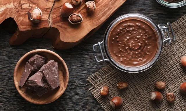 Zutaten für Nuss-Nougat-Creme selber machen: Haselnüsse, Schokolade und ein Glas voller Genuss.